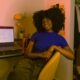 Black female content creator smiling at the camera sitting in a room with her laptop and light ring