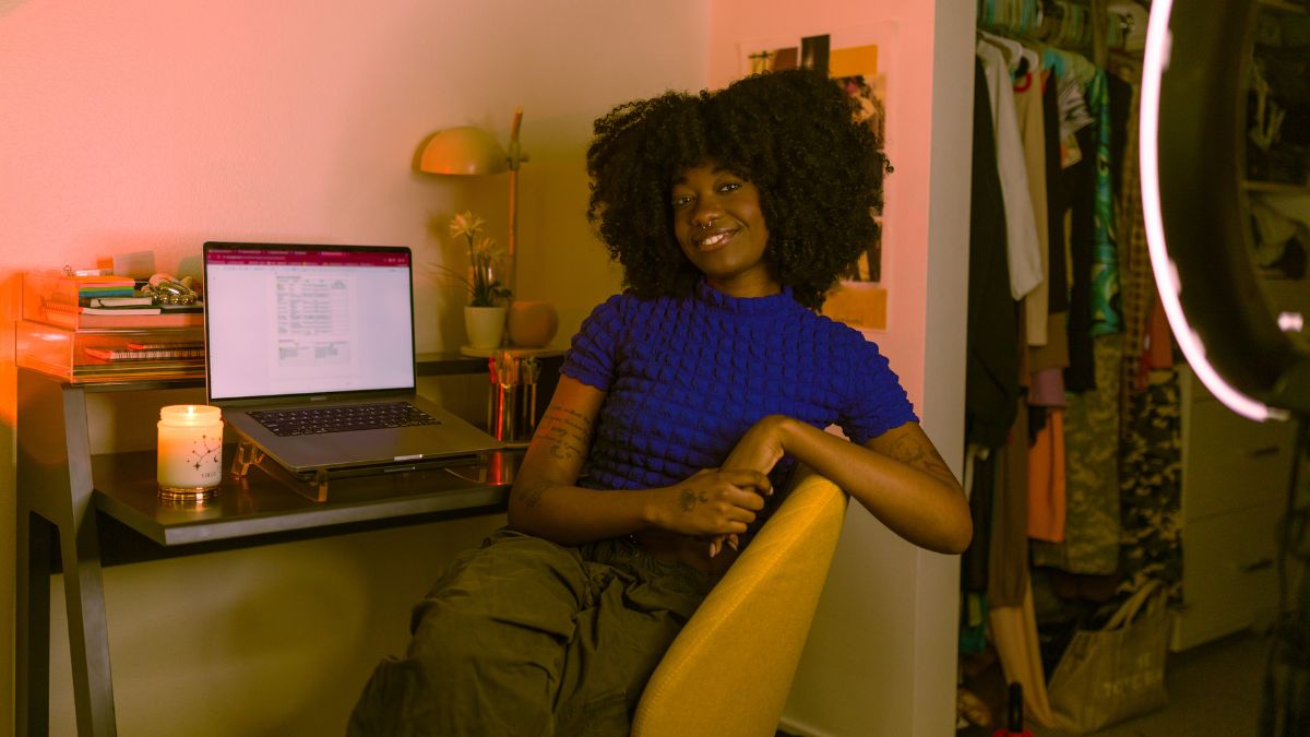 Black female content creator smiling at the camera sitting in a room with her laptop and light ring