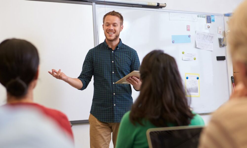Male teacher smiling in front of the class students and explaining
