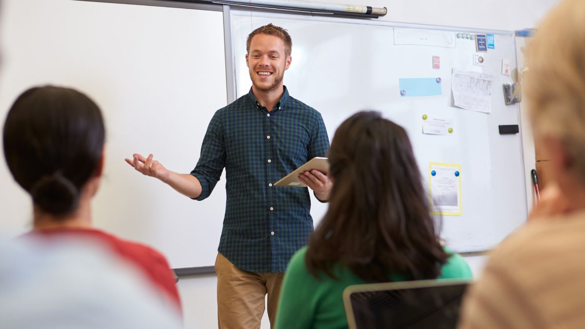 Male teacher smiling in front of the class students and explaining