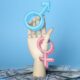 A mannequin hand holding up the male and female symbols with a pile of money strewn around