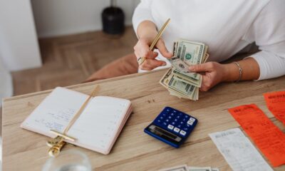 Closeup of a women's hands counting money next to a calculator, receipts, and open notebook