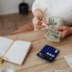 Closeup of a women's hands counting money next to a calculator, receipts, and open notebook